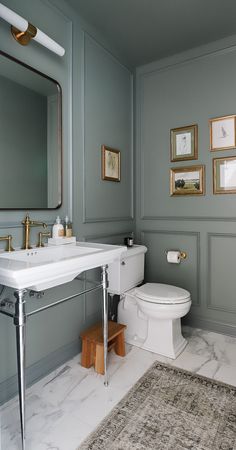 a white toilet sitting next to a sink in a bathroom under a mirror and framed pictures on the wall