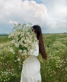 a woman in a white dress is walking through a field with daisies