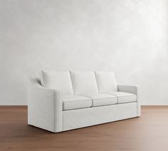 a white couch sitting on top of a hard wood floor next to a wall and window