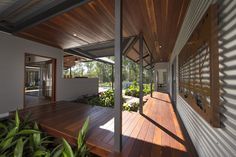 a house with wooden flooring and large windows on the side of it, surrounded by greenery