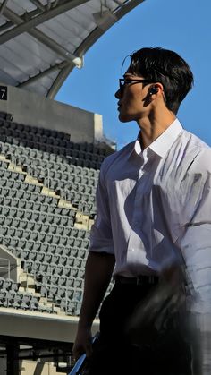 a man wearing glasses and a white shirt is standing in front of a stadium bleachers