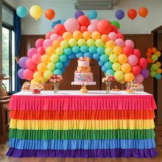 there is a rainbow cake and balloons on the table