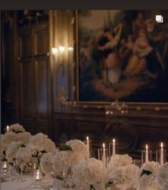 a long table with white flowers and candles in front of a painting on the wall