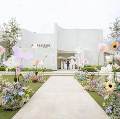 a couple standing in front of a white building with flowers on the lawn and walkway