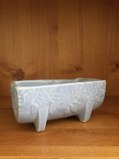 a white ceramic planter sitting on top of a wooden shelf next to a wall