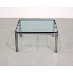 a glass and metal coffee table on concrete flooring with white walls in the background