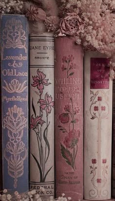 some books are lined up on a shelf with flowers in the middle and one is pink