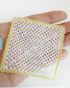 a hand holding a small yellow and white doily