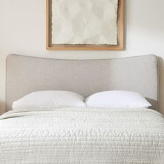 a bed with white pillows and a painting above it