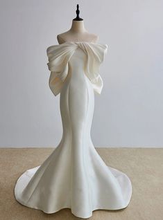 the back of a white dress on a mannequin head stand in front of a wall