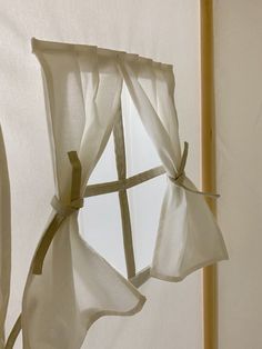 a white curtain hanging from the side of a window with two ties attached to it