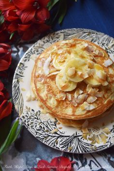 a plate topped with pancakes covered in toppings next to red flowers on a blue table cloth