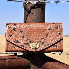 Large tan embossed leather wallet in floral and basket weave prints and painted black detailing. Brass toggle clasp closure on the envelope front flap. Womens Western Hats, Western Bracelets, Tooled Leather Bag, Leopard Bag, Leather Weekender Bag, Leather Weekender, Rugged Leather, Leather Patchwork, Western Hats