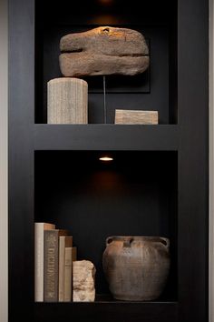 some books and vases in a black bookcase with rocks on the bottom shelf