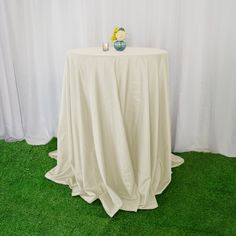 a round table with a white cloth draped over it and vases on the top