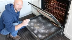 a man kneeling down in front of an open oven with something on the bottom shelf