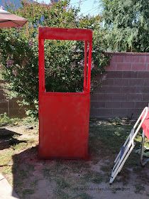 a red trash can sitting in the middle of a yard next to a chair and table