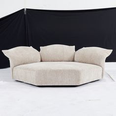 a round couch sitting on top of a white floor next to a black wall and chair