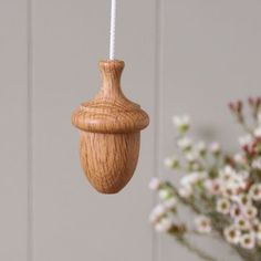 a wooden ornament hanging from a white string with flowers in the back ground