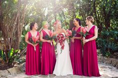 a group of women standing next to each other in front of trees and bushes with flowers