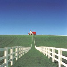 a white fence with a red barn in the distance and a green field behind it