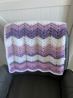 a purple and white crocheted blanket sitting on top of a black leather chair