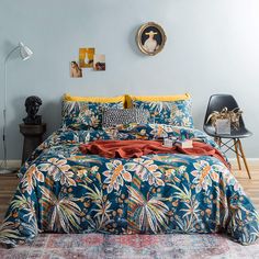 a bed with blue and yellow comforter in a bedroom next to a chair, lamp and pictures on the wall