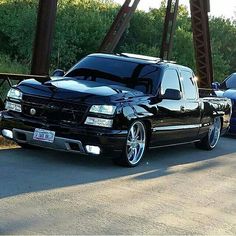 two black trucks parked on the side of a road next to each other in front of a bridge