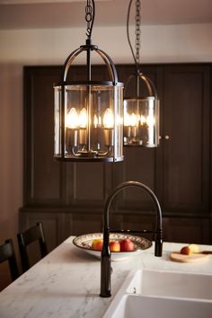 a light fixture hanging over a kitchen counter top next to a bowl of fruit on a plate