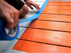 a person is using a blue tape to paint the wooden floor with an orange color