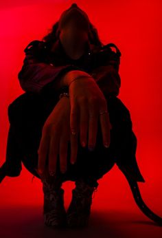 a woman sitting on the ground with her hands over her face, in front of a red background