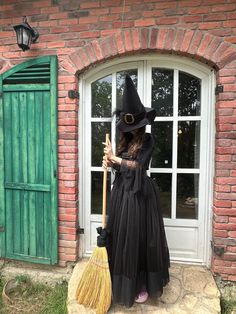 a woman dressed as a witch holding a broom and standing in front of a brick building