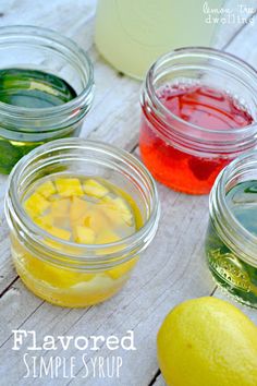 four jars filled with different colored liquids next to a lemon and an orange slice