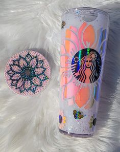 a starbucks cup next to a pink and blue flower on a white furnishing