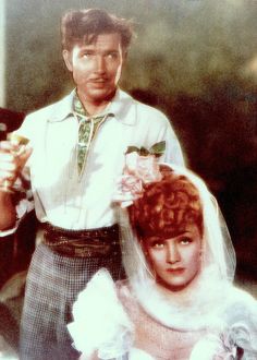 a man and woman standing next to each other in front of a building with flowers on their hair