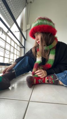 a woman sitting on the floor with her legs crossed wearing a hat and holding a stuffed animal