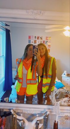 two women in safety vests are taking a selfie with their cell phone while standing in front of a mirror