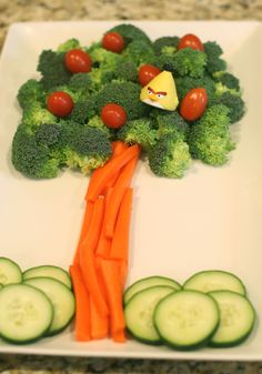 a white plate topped with cucumbers and carrots next to a tree made out of broccoli