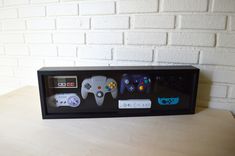 a display case with four different video game controllers in front of a white brick wall