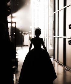 a black and white photo of a woman in a dress walking down a hall way