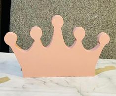 a pink wooden crown sitting on top of a white marble table next to a wall