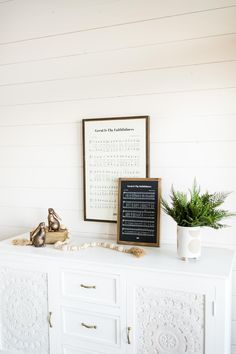 a white dresser with a chalkboard on it and a potted plant next to it