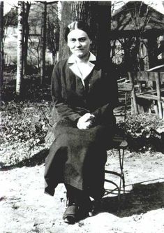 an old black and white photo of a woman sitting on a chair next to a tree