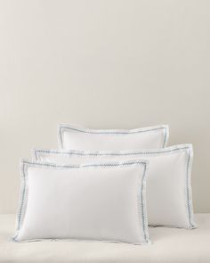 three white pillows on a bed with blue trimmings and an embroidered pillow case