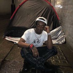 a man sitting on the ground in front of a tent with chains around his ankles