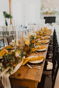 a long table with yellow flowers and candles on it is set for a formal dinner