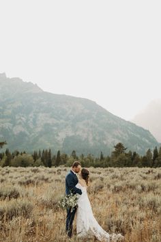 a bride and groom standing in the middle of a field with mountains in the background