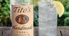 a bottle of vodka next to a glass filled with ice and lemon wedges on a wooden table