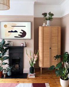 a living room filled with lots of plants next to a fire place and a painting on the wall