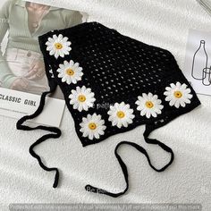 a crocheted hat with white daisies on it next to a book and magazine